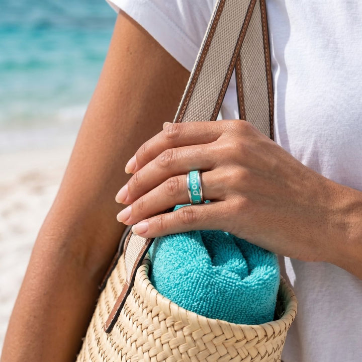 Bague mood portée par une femme avec manucure parfaite sur une plage avec le logo blanc et l'anneau interchangeable turquoise