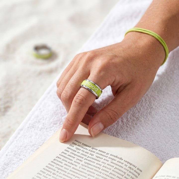 Bague mood portée par une femme avec manucure parfaite sur une plage avec le logo blanc et l'anneau interchangeable vert mood