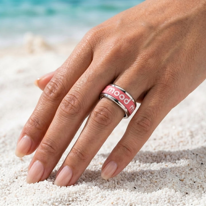 Bague mood portée par une femme avec manucure parfaite sur une plage avec le logo blanc et l'anneau interchangeable rose